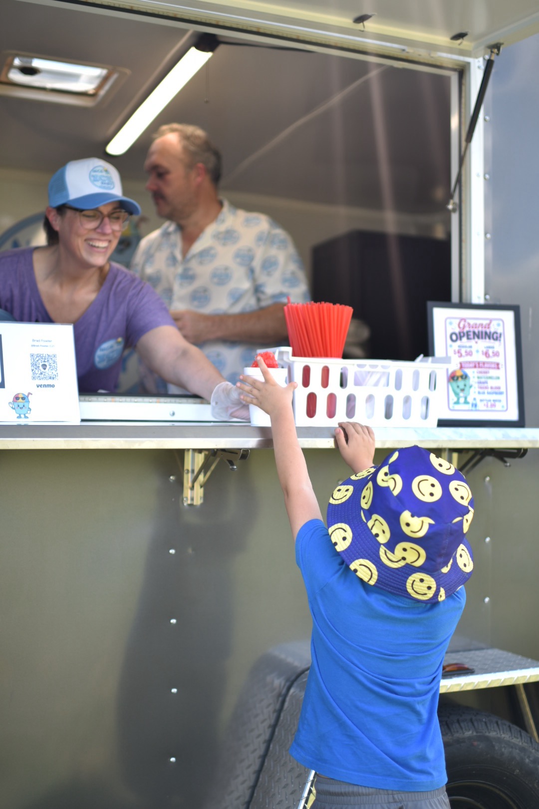 A child reaching up to receive a snowcone from the Nice Ice Baby truck